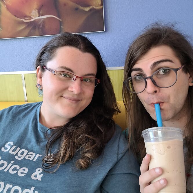 Two people smiling in cafe, one drinking smoothie